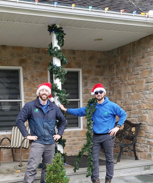 Two-holiday lighting professionals standing in front of a house.
