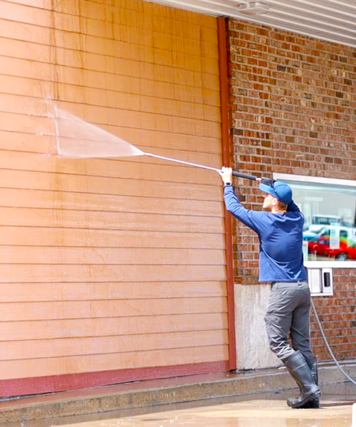 A man is pressure washing house siding.