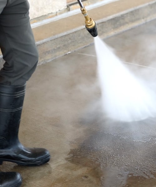 A man is using a hose to pressure wash the concrete floor.