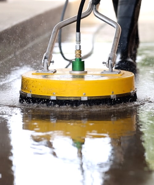 Power washing technician using a circular surface cleaner to wash concrete.