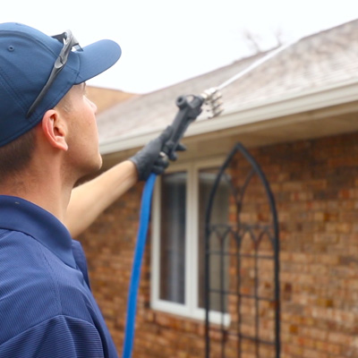 roof washing professional spraying roof in blue hat