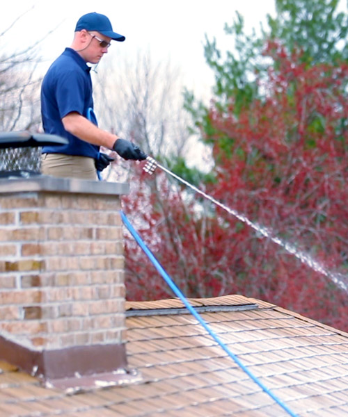 roof washing professional spraying roof in blue shirt