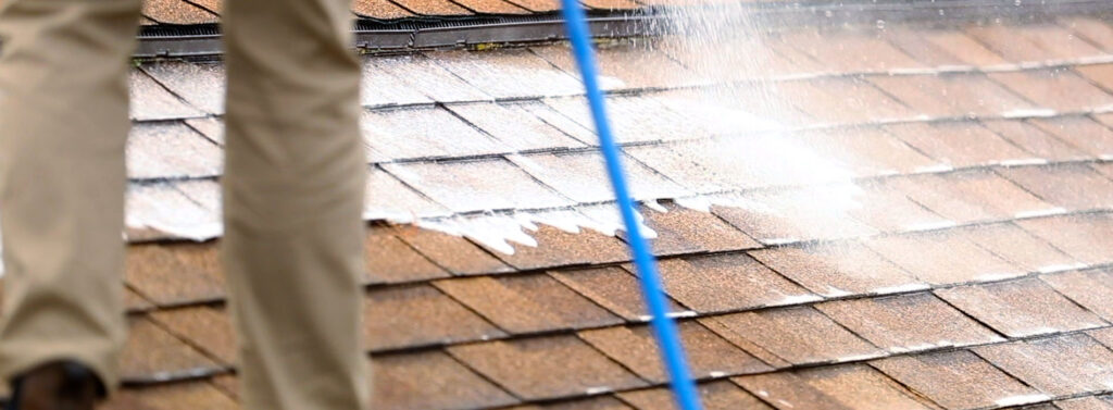 professional in brown pants standing on roof and spraying at soap